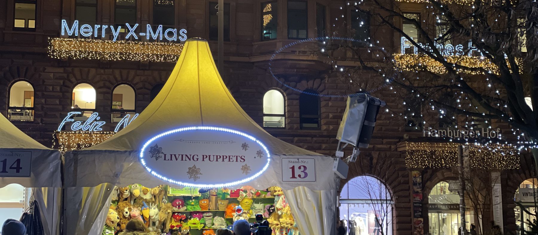 Stand Living Puppets, Stand-Nr. 13, vor weihnachtlich beleuchteter Fassade am Jungfernstieg